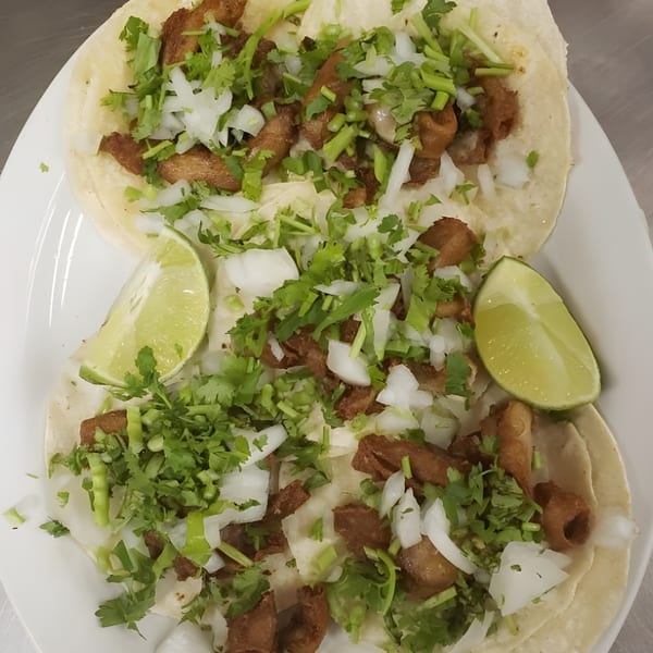 Three Albertano's Mexican tacos with meat, cilantro, onions, and lime wedges on a white plate.