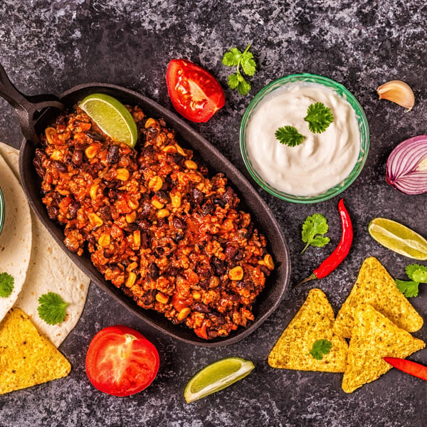 Albertano's Mexican chili in a skillet with tortillas, nachos, sour cream, and fresh ingredients.